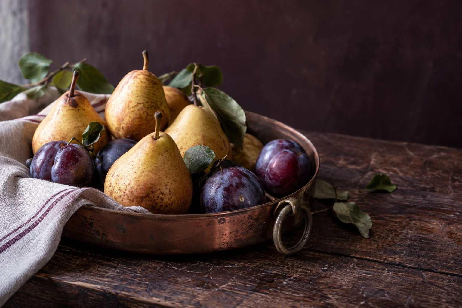 Poires et prunes sur un plateau en cuivre, dans une lumière naturelle.